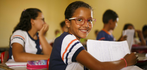 várias crianças concentradas enquanto uma menina sorri virando uma folha de caderno e olhando para a câmera dentro de uma escola no sertão do piauí