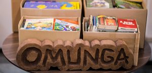 vários livros em caixas abertas com um pedaço médio de madeira com a logo da omunga que busca ter projetos incentivados pela lei rouanet